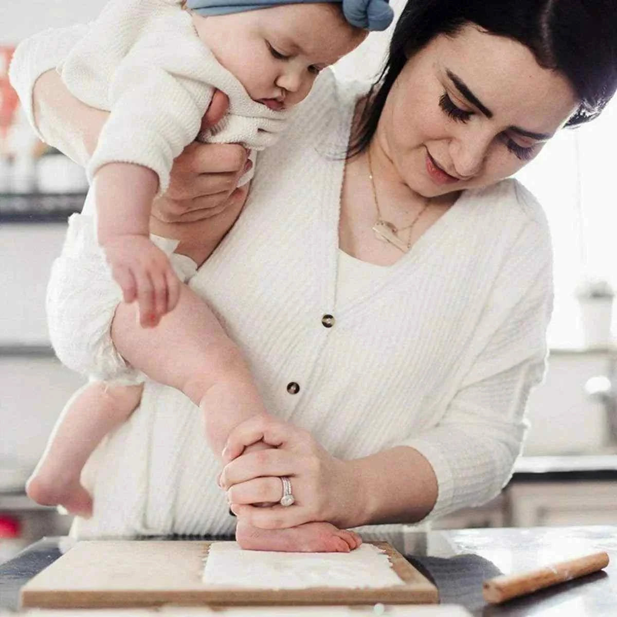 DIY Baby Print keepsake set with a baby’s foot pressed into white clay on a wooden board, with a rolling tool nearby.